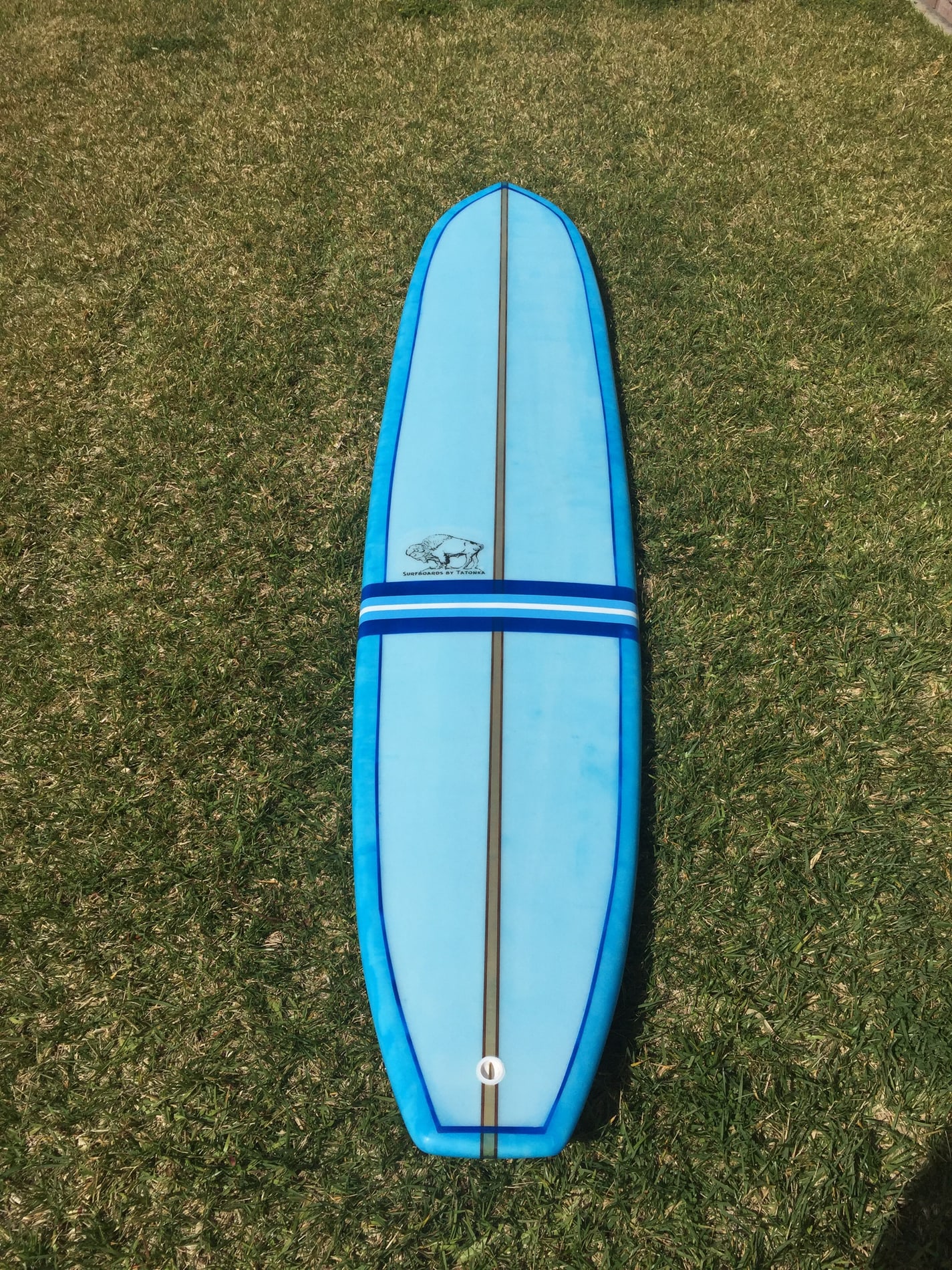 Blue striped Tatonka surfboard deck resting on grass