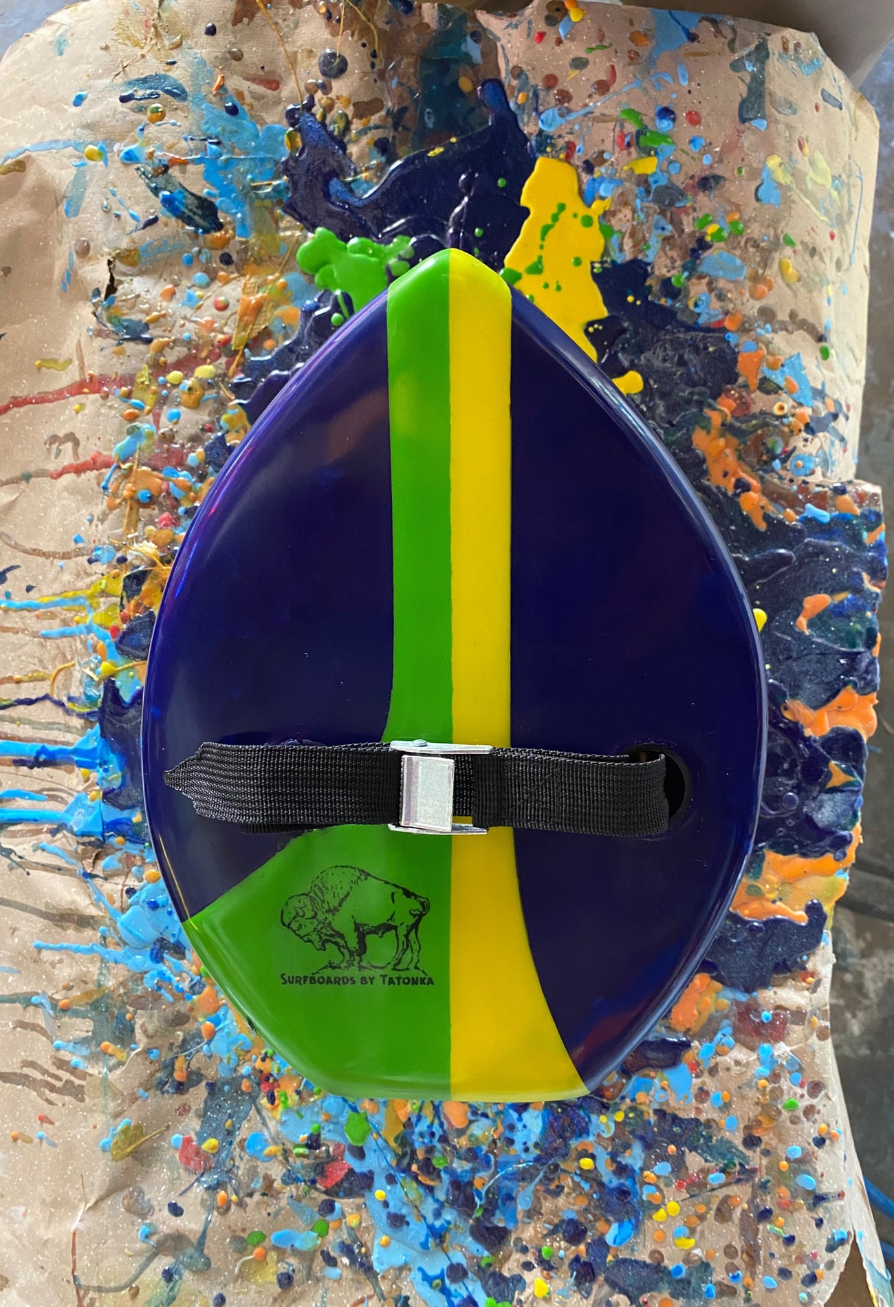 Purple green and yellow handplane with a black strap on a colorful workbench