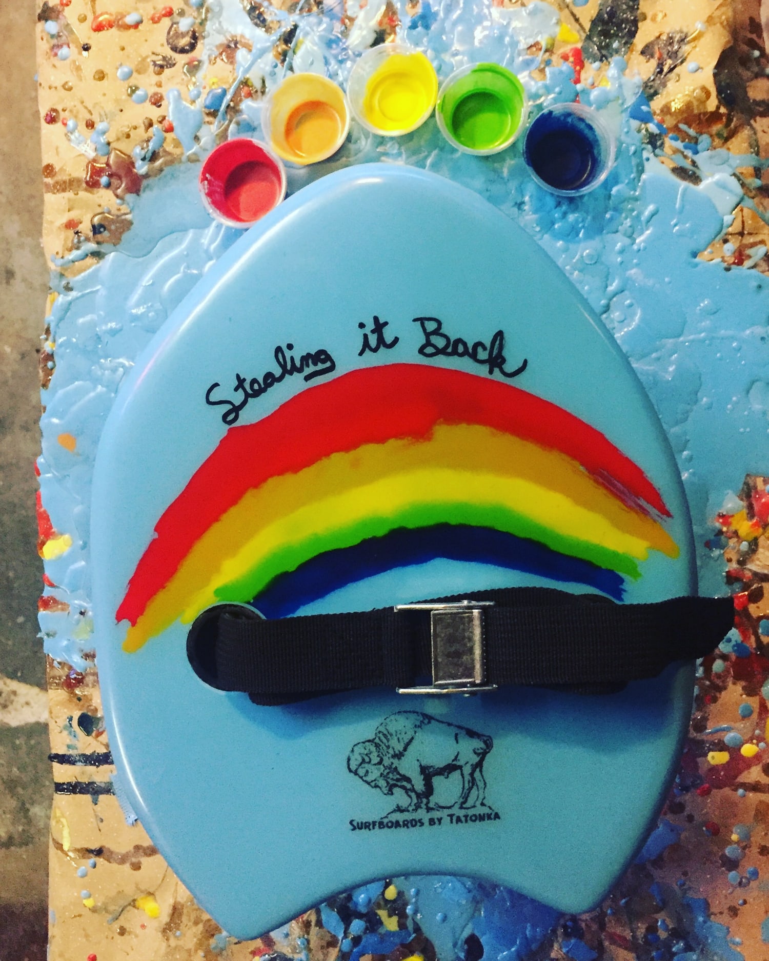 Blue rainbow handplane beside cups of bright color