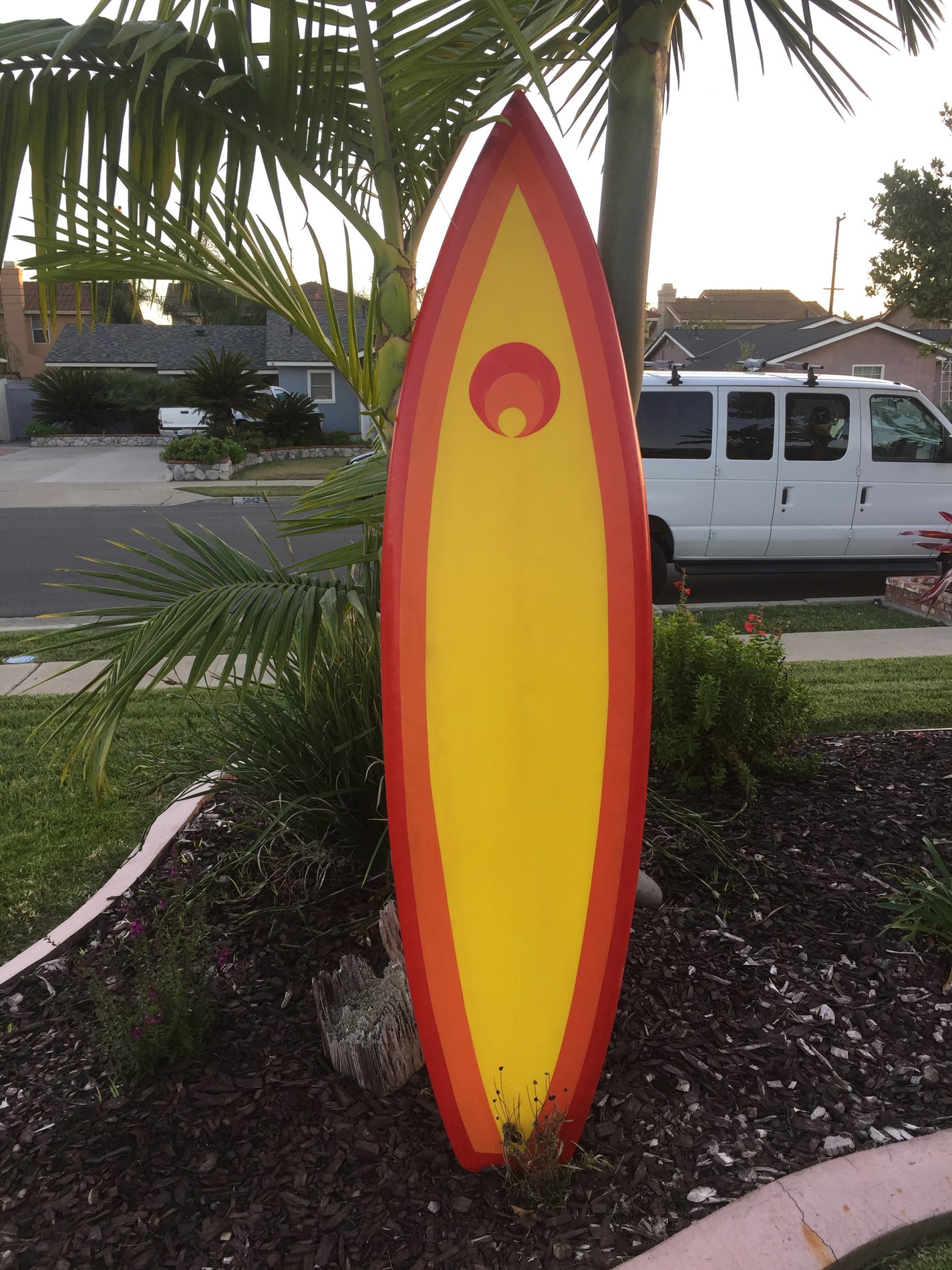 Yellow and orange Tatonka surfboard standing beneath palm leaves