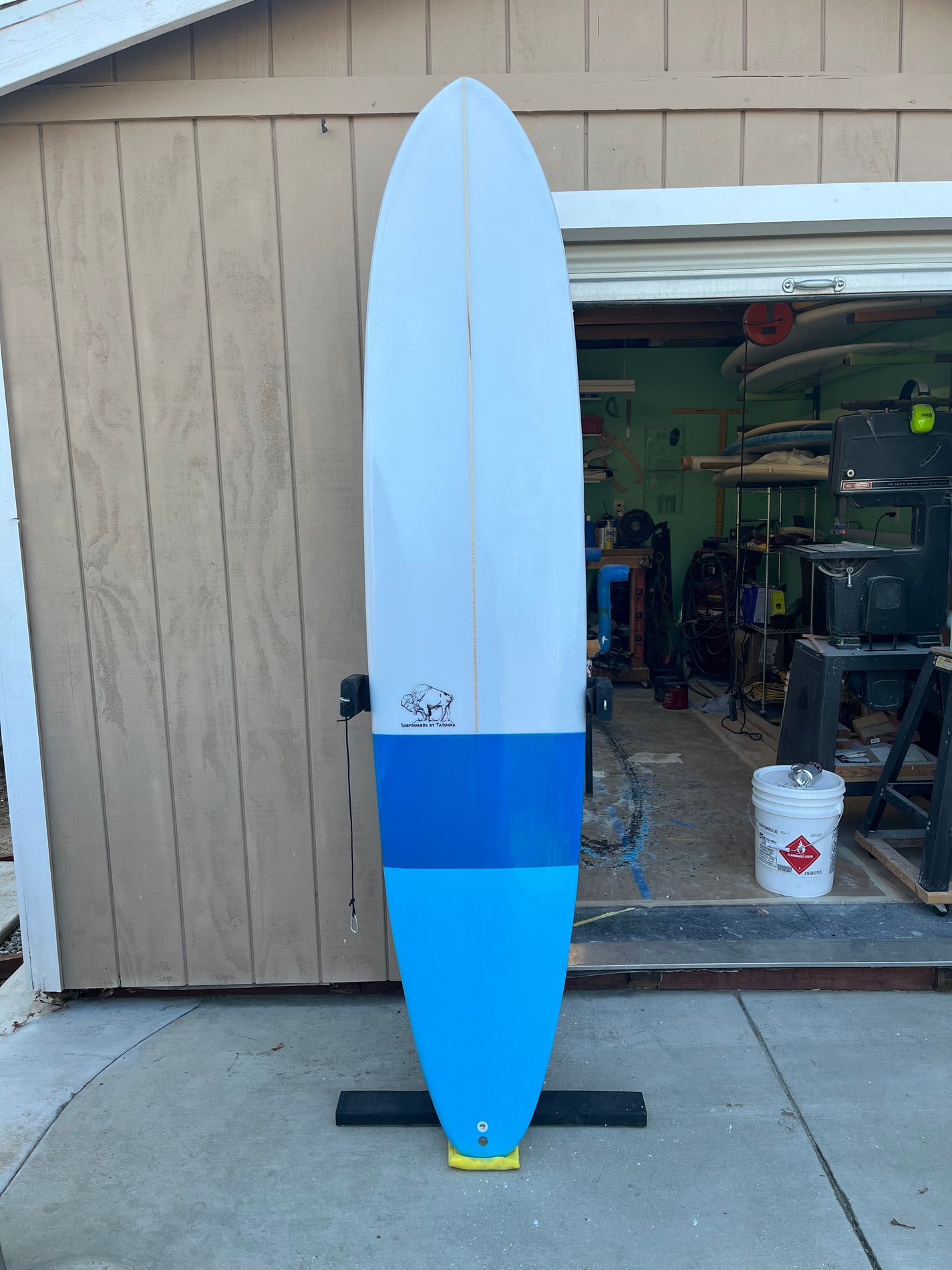Blue and white Tatonka surfboard standing outside the workshop